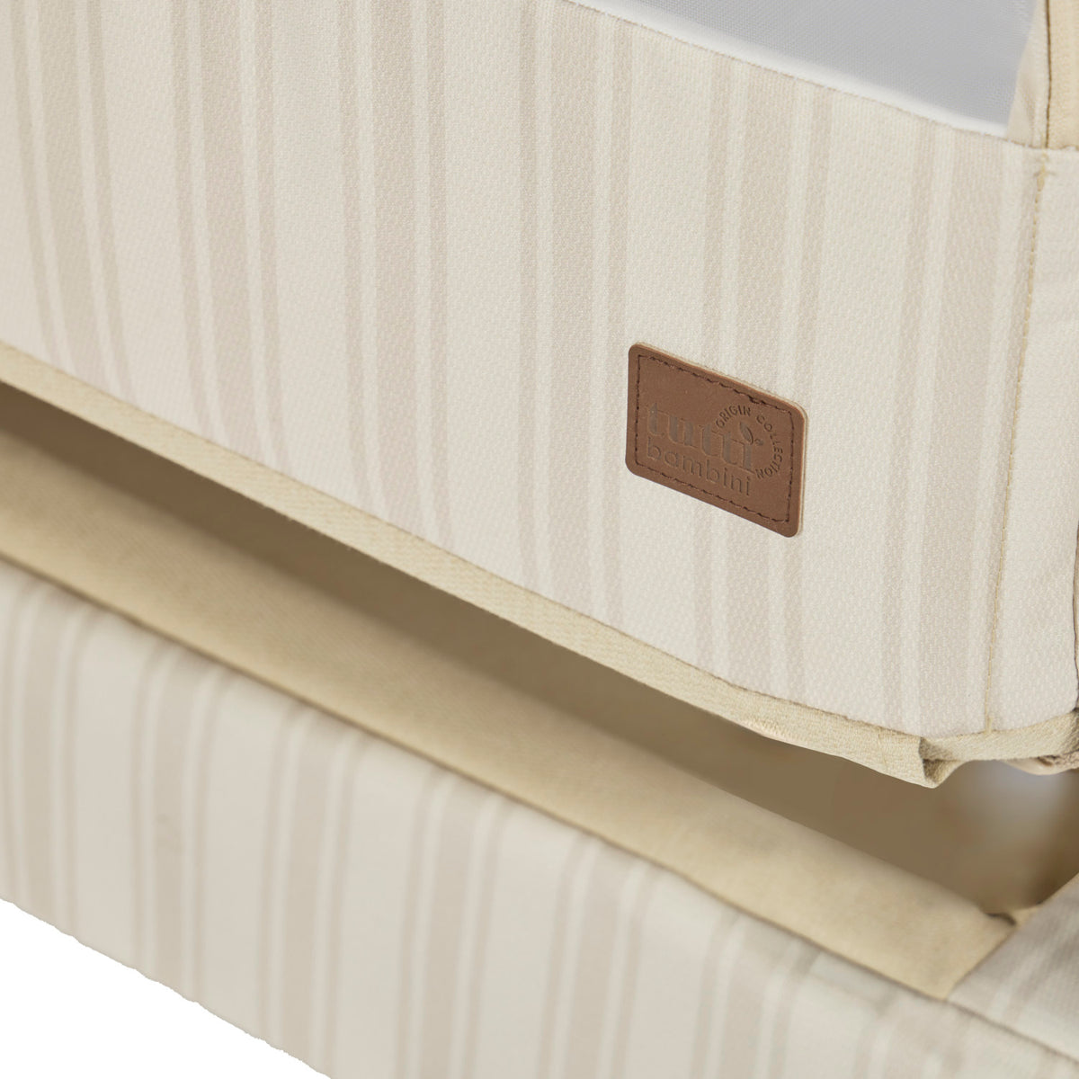 A close up view of the CoZee Air 2 bedside crib in rich walnut and cashmere vintage stripe showing the Origin logo stitched onto the side corner of the crib.