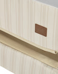 A close up view of the CoZee Air 2 bedside crib in rich walnut and cashmere vintage stripe showing the Origin logo stitched onto the side corner of the crib.
