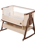 A baby bedside crib with a cream-colored striped fabric body and a dark brown wooden frame, shown on a white background.