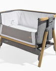 Cutout view of the CoZee bedside crib in charcoal and oak with mesh side panel unzipped, showing breathable liner and wooden frame