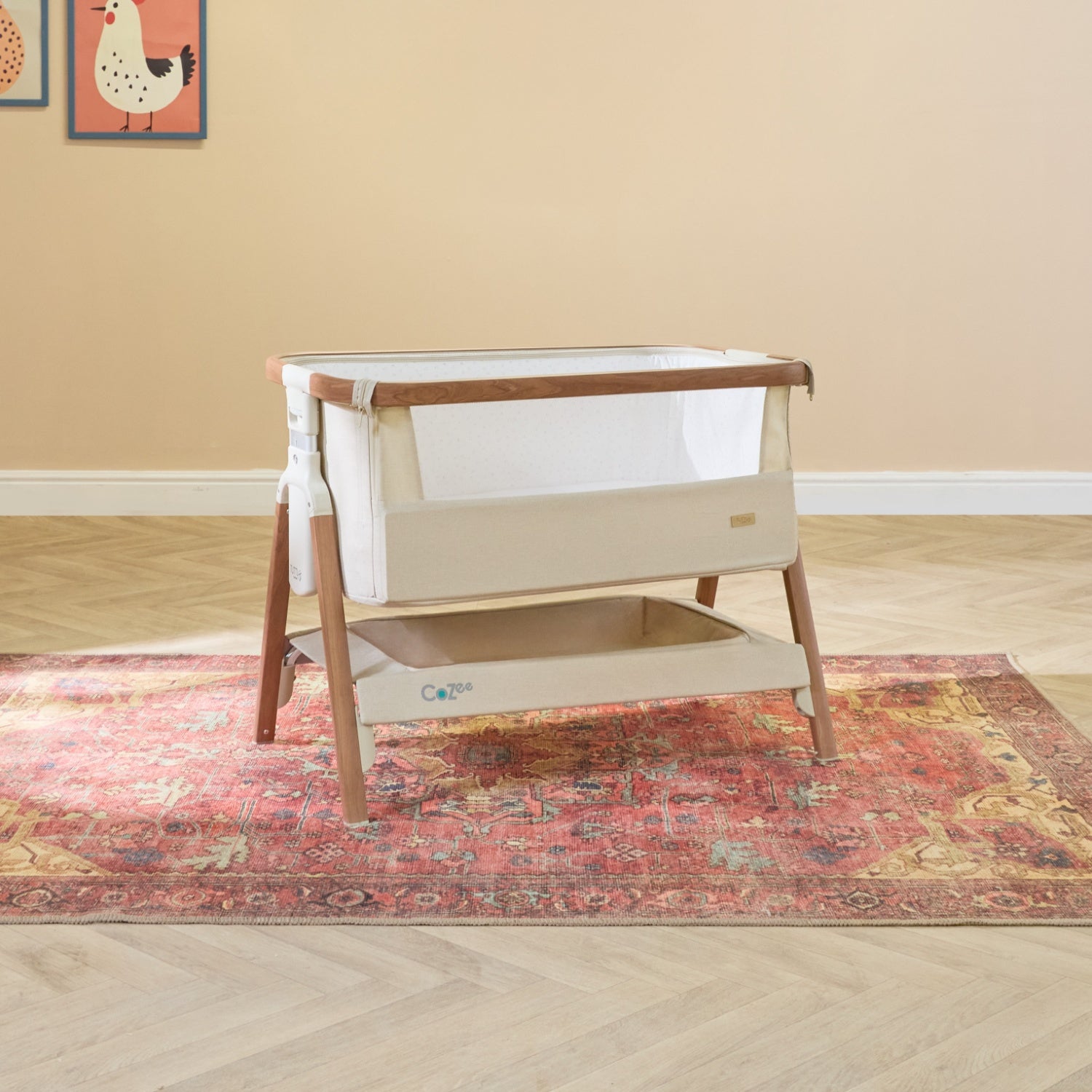 CoZee bedside crib in Scandinavian walnut set in a warm nursery, showing breathable mesh sides and spacious under-crib storage