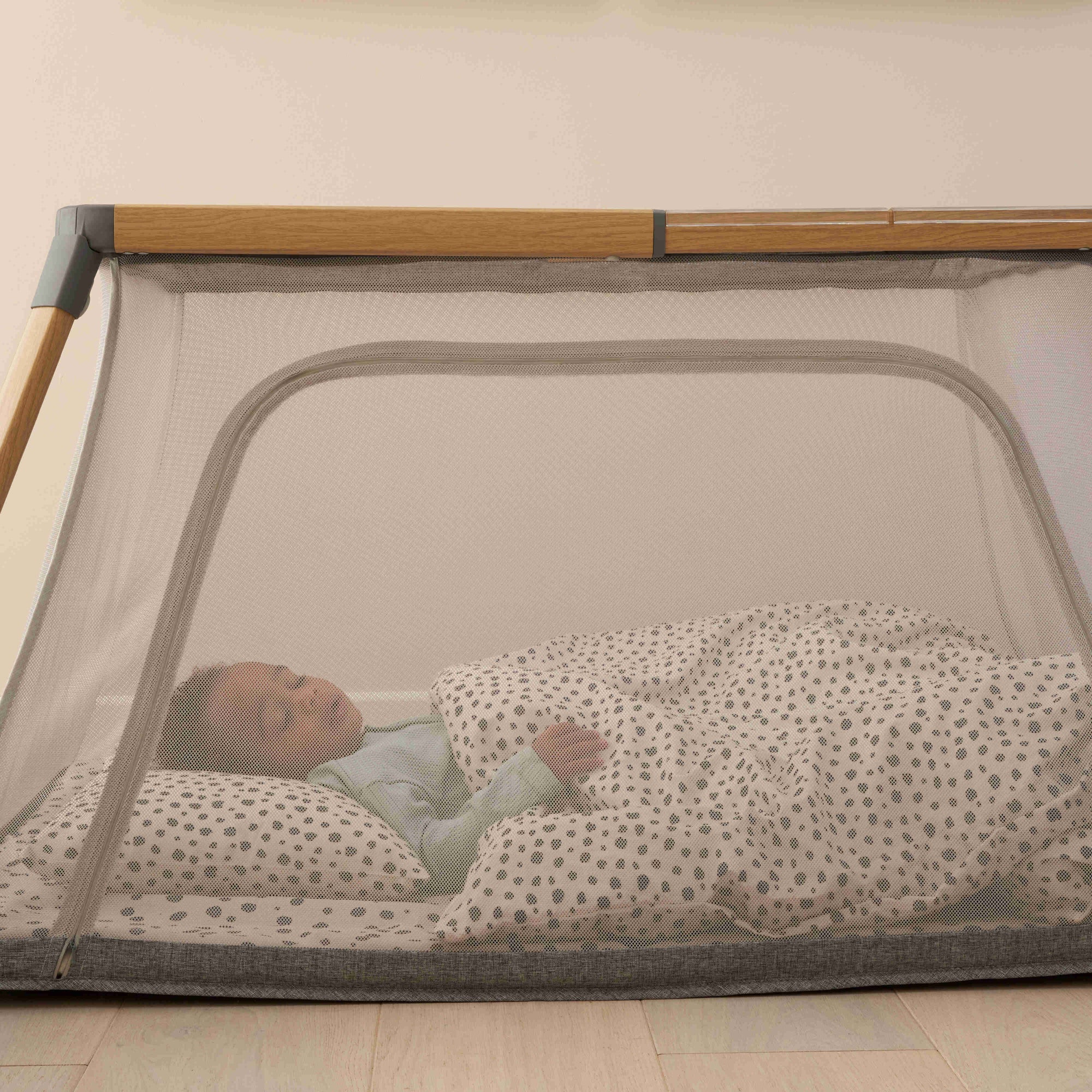 Side view of the CoZee Go travel cot with breathable mesh panels, showing a baby sleeping comfortably while allowing airflow and easy visibility