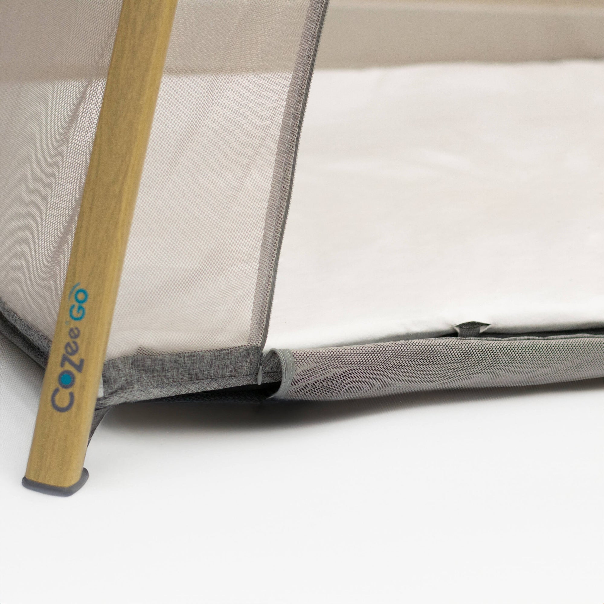 Crib with a wooden support and mesh side, featuring the Cozee Go brand.