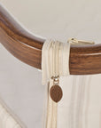 A close-up of a cream-colored zipper with a brown leaf-shaped pull tab, representing Origin, attached to a curved dark brown wooden frame, with a white mesh panel below.