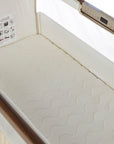 A close-up of a cream-colored mattress with a wavy quilted pattern, shown inside a bedside crib. A control panel is visible on the side rail, and an instruction sheet is attached to the inner wall.