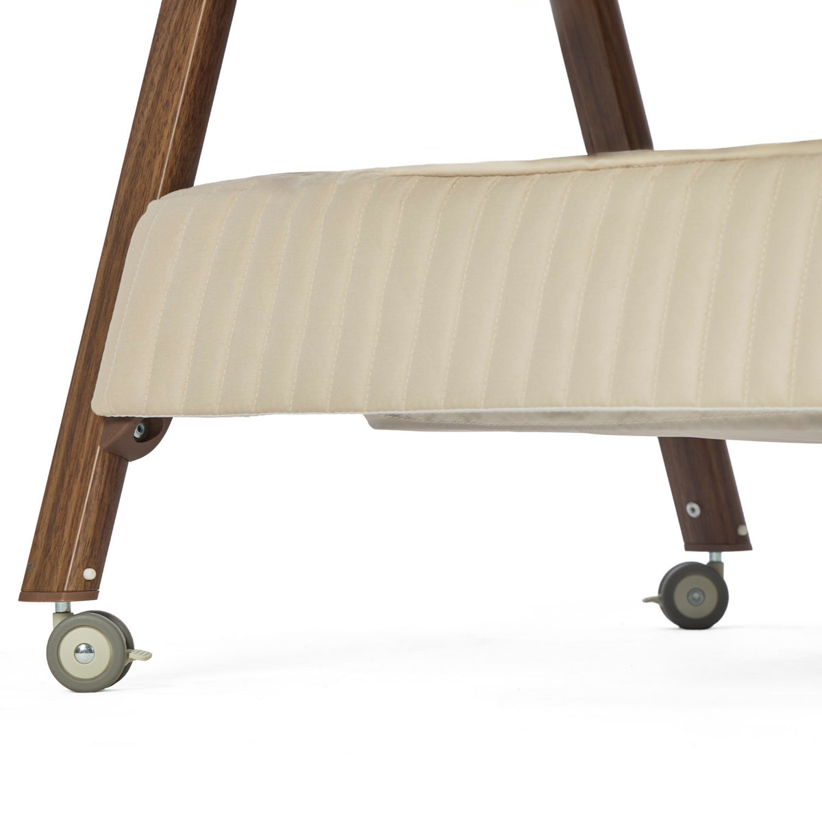 Close-up of a mobile bedside crib frame with a  quilted cashmere fabric, dark walnut wooden legs, and gray caster wheels on a white background.