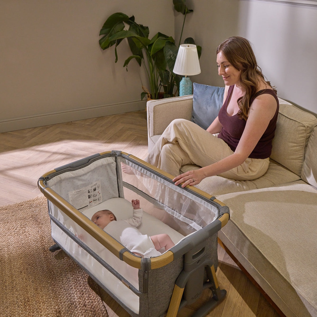 Baby rests peacefully in the CoZee XL Oak/Charcoal in Bassinet Mode, with mesh sides for airflow and parent seated nearby