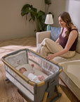 Baby rests peacefully in the CoZee XL Oak/Charcoal in Bassinet Mode, with mesh sides for airflow and parent seated nearby