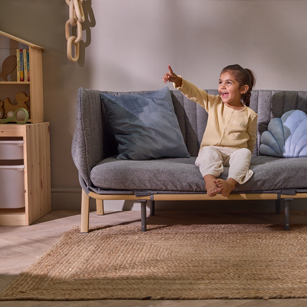 Smiling child points excitedly while sitting on the CoZee XL in oak and charcoal set up in sofa bed mode