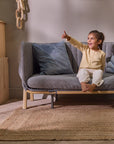 Smiling child points excitedly while sitting on the CoZee XL in oak and charcoal set up in sofa bed mode
