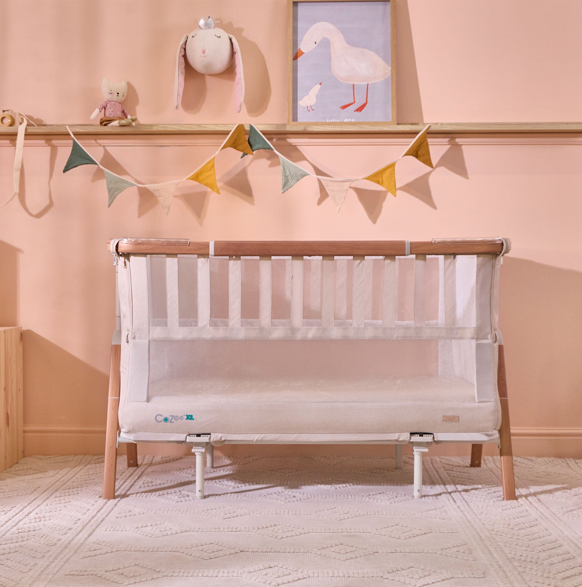 Styled nursery view of the CoZee XL Scandi cot with mesh sides, set against soft pink walls with bunting and framed art