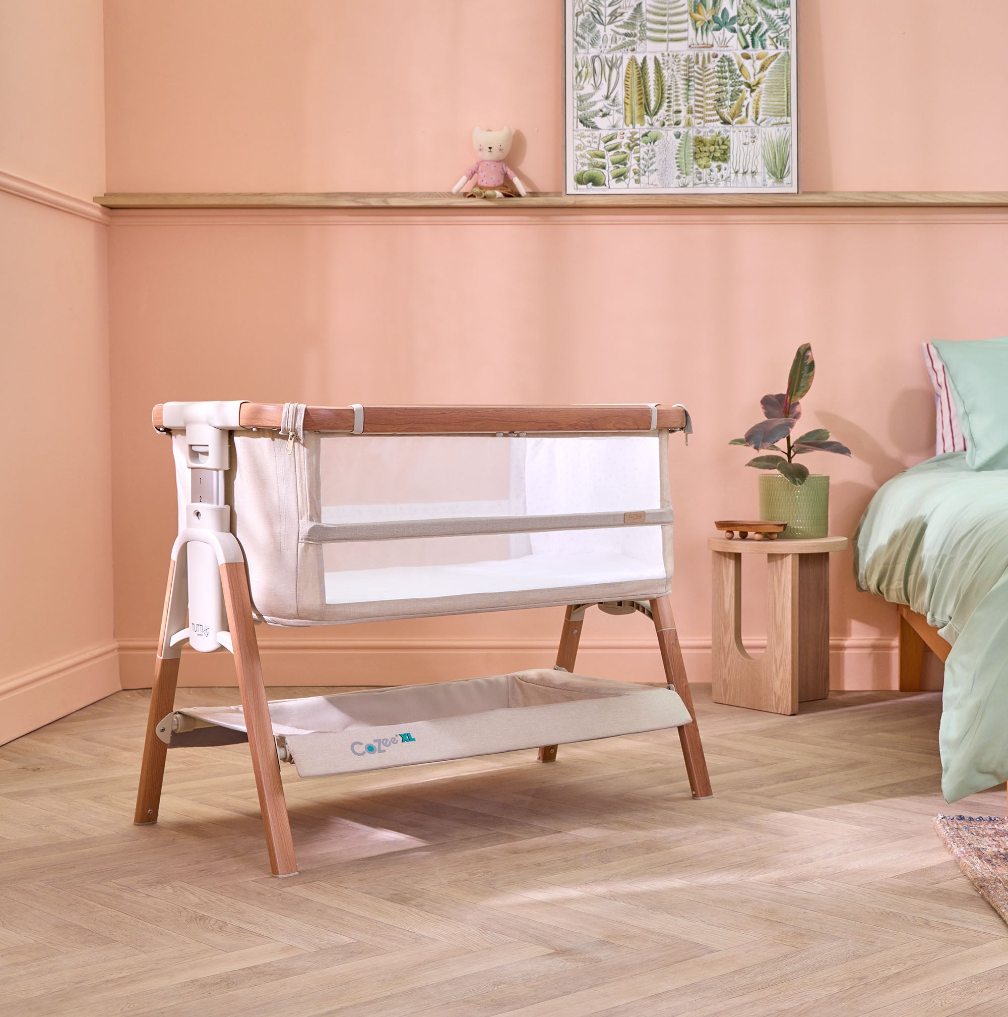 Angled view of the CoZee XL Scandi bedside crib with mesh sides and under-crib storage basket, styled in a soft, calming bedroom setting