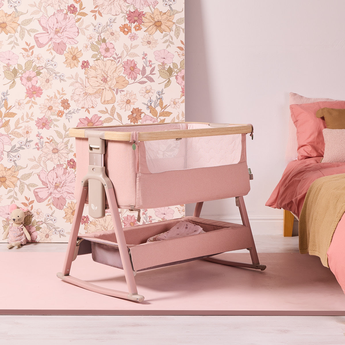 Angled lifestyle view of the CoZee Air 2 bedside crib in blush, highlighting rocking legs and soft fabric finish.