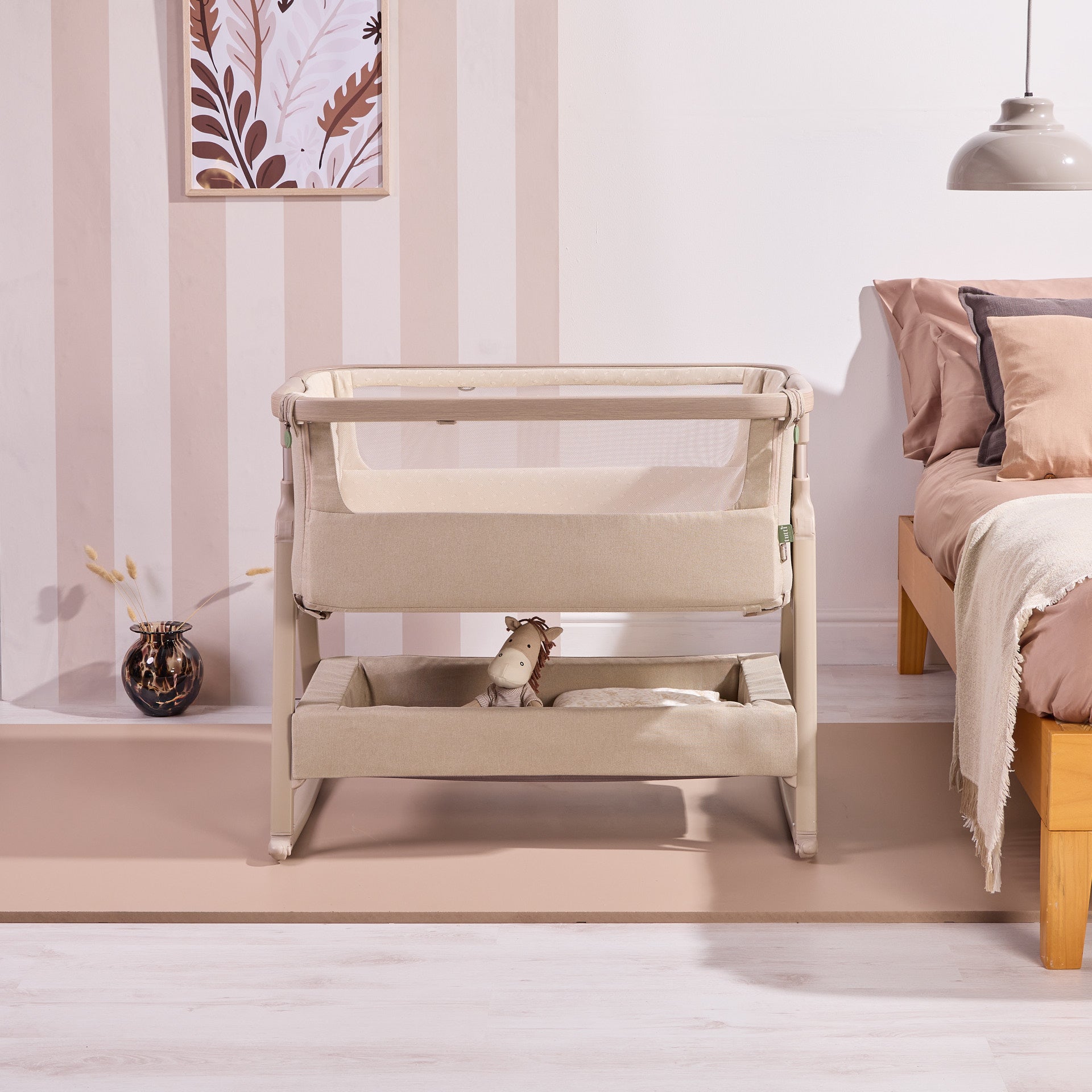 Lifestyle view of the CoZee Air 2 in cocoa beside the bed, showing breathable mesh sides and integrated storage basket below.