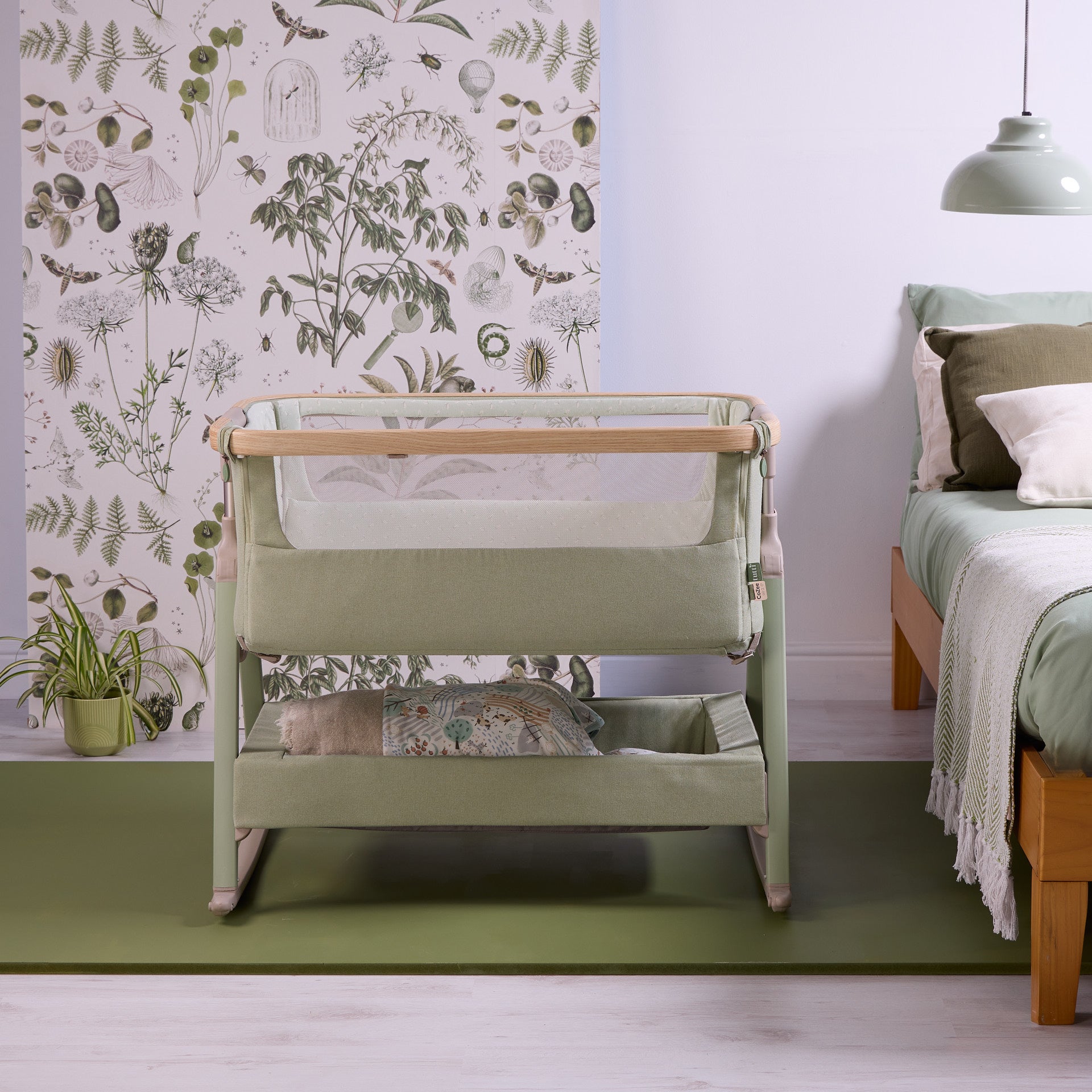 Front view of the CoZee Air 2 bedside crib in eucalyptus, styled beside the bed with mesh panels and integrated storage shelf.