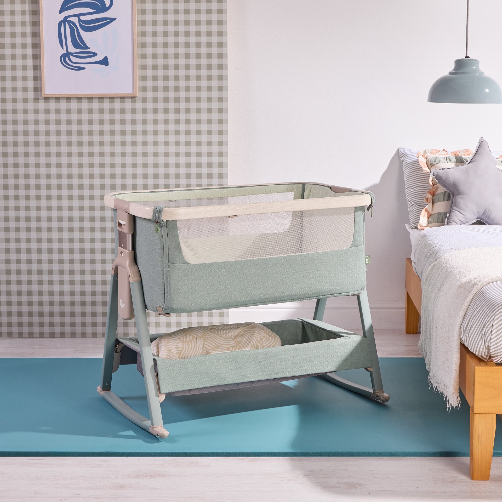 Angled room view of the cozee air 2 bedside crib in kelp and whitewash, highlighting soft green fabric and integrated storage basket.