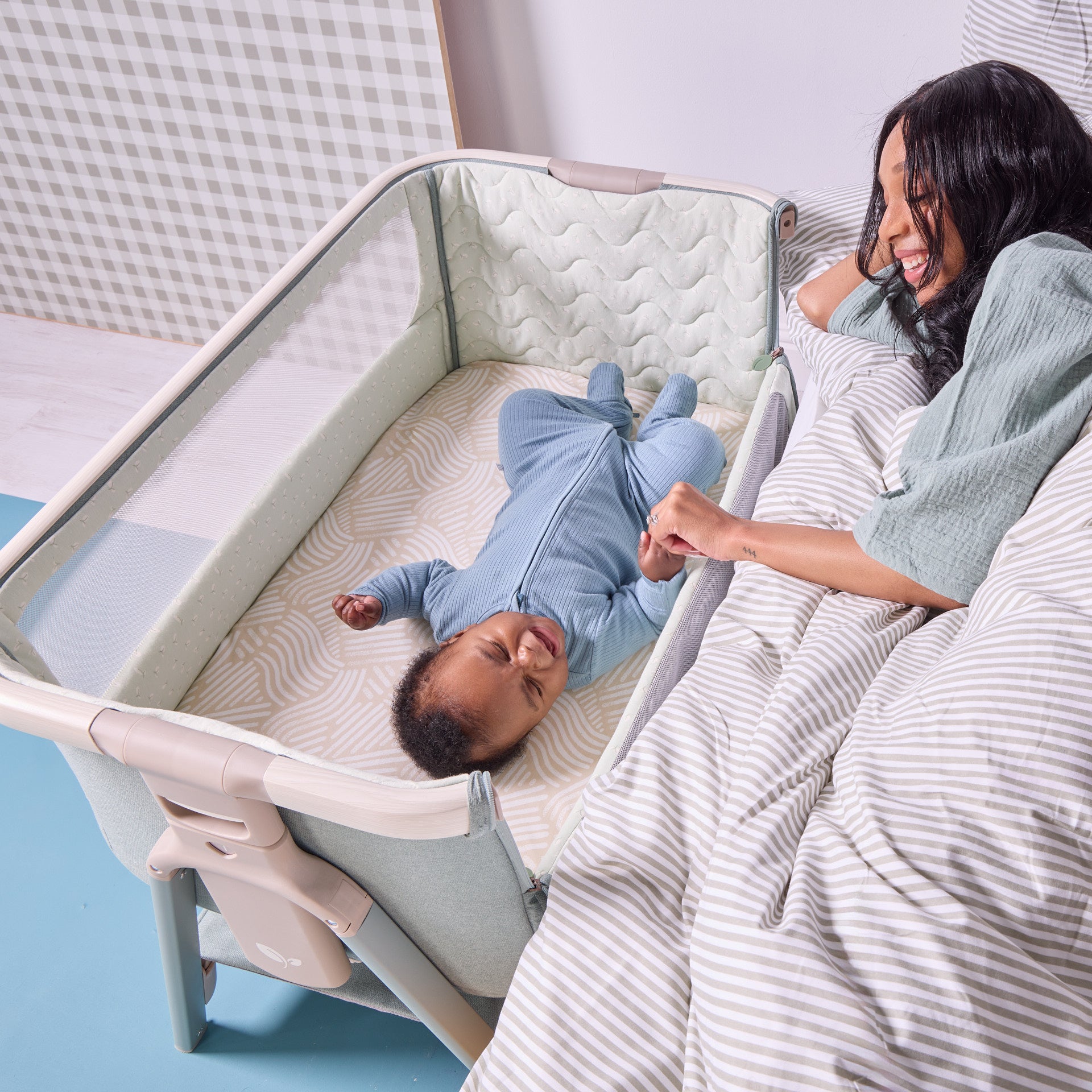 Parent and baby lifestyle image of the cozee air 2 bedside crib in kelp and whitewash, showing easy access and close interaction during night-time settling.