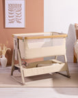 Styled nursery scene featuring the CoZee Air 2 bedside crib in toasted oak/sand with soft textiles and calm, neutral tones.