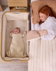 Overhead view of baby sleeping in the CoZee Air 2 bedside crib in toasted oak/sand positioned neatly beside the bed.