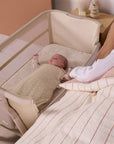 Baby resting beside parent in the CoZee Zen in sand bedside crib, highlighting safe co-sleeping positioning and breathable mesh sides.