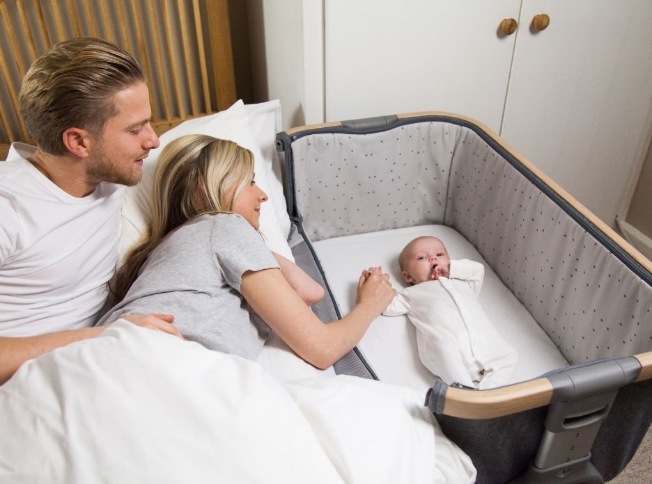 Father and mother next to a baby on a CoZee Bedside Crib