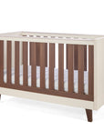 An angle view of the Como cot bed in cashmere and rich walnut, featuring wooden slate slats in a sturdy, modern frame.