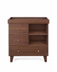 A front view of the Como chest changer in walnut with a removable changing top, three drawers and open shelving for organised nursery storage.