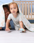 Parent and toddler sharing a playful moment beneath the Good Life cot bed coverlet, showcasing its soft texture and calming colours