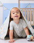 Toddler playing under the Good Life cot bed coverlet, smiling brightly while wrapped in its soft countryside inspired quilted fabric