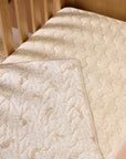 Love Cats cot bed coverlet styled inside wooden cot, featuring reversible beige animal print and soft quilted finish for cosy comfort.
