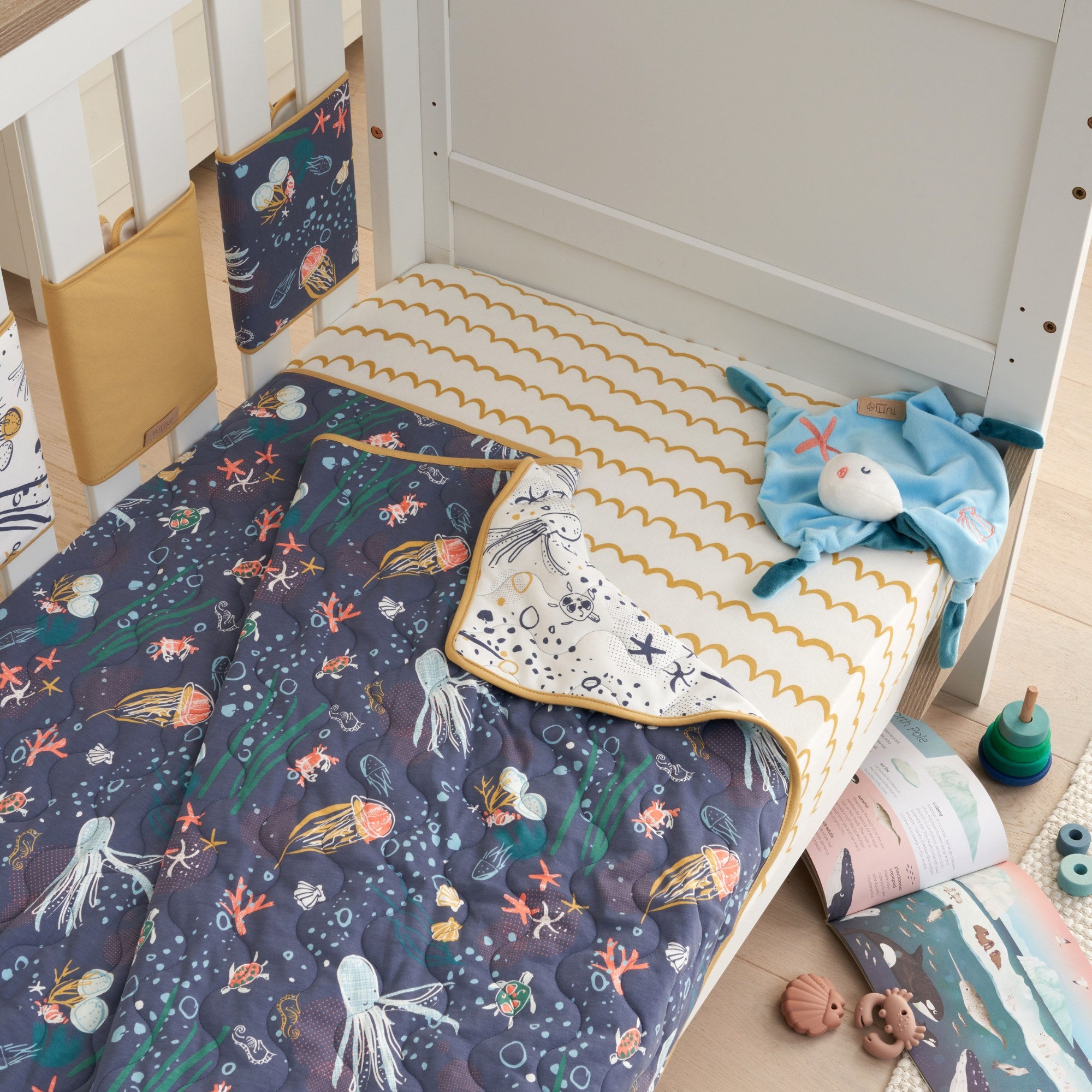 cot bed in sofa bed mode styled with the Our Planet cot bed coverlet, featuring quilted texture and nature-inspired print in a cosy nursery setting.