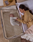 Overhead view of baby lying in CoZee Sense bedside crib as mother gently reaches through open side panel.