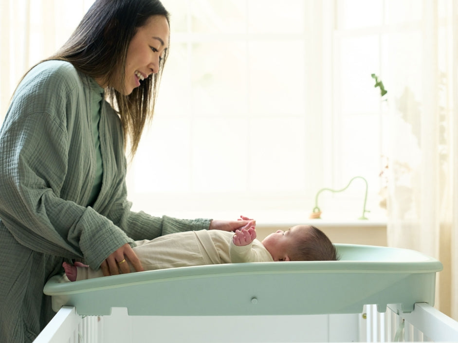 Mum gently changing baby on the Cushi baby changing mat, showing raised sides and supportive, wipe-clean design.