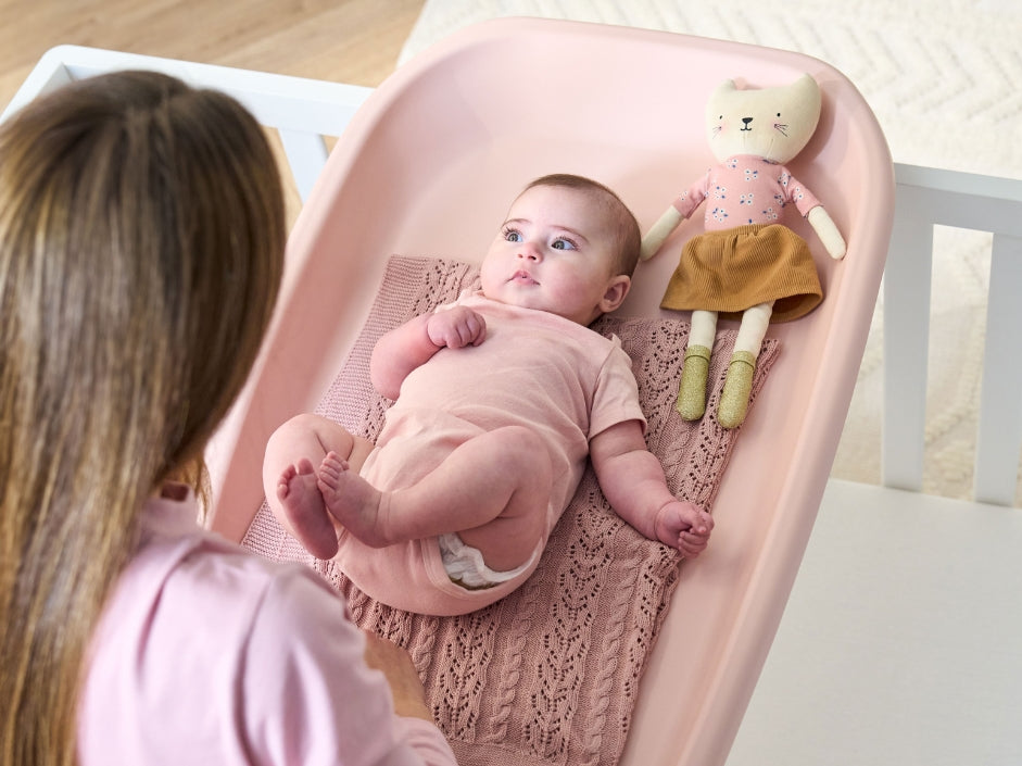 Overhead lifestyle view of the Cushi baby changing mat in petal, showing a baby resting comfortably during a calm, supported nappy change