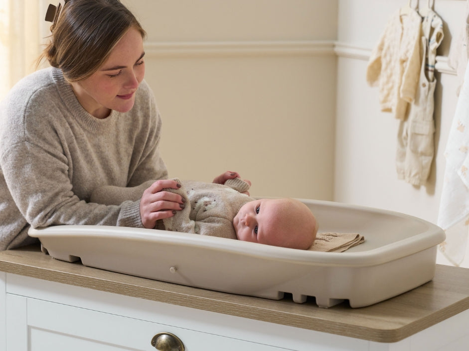 Baby lying comfortably on the Cushi baby changing mat, styled on a chest changer with softly raised edges.