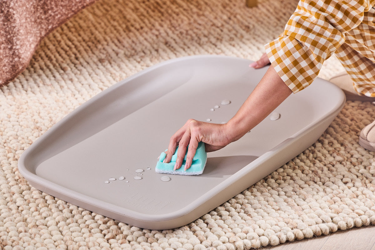 Lifestyle image showing the Cushi Mini changing mat being wiped clean, highlighting its easy-clean surface.