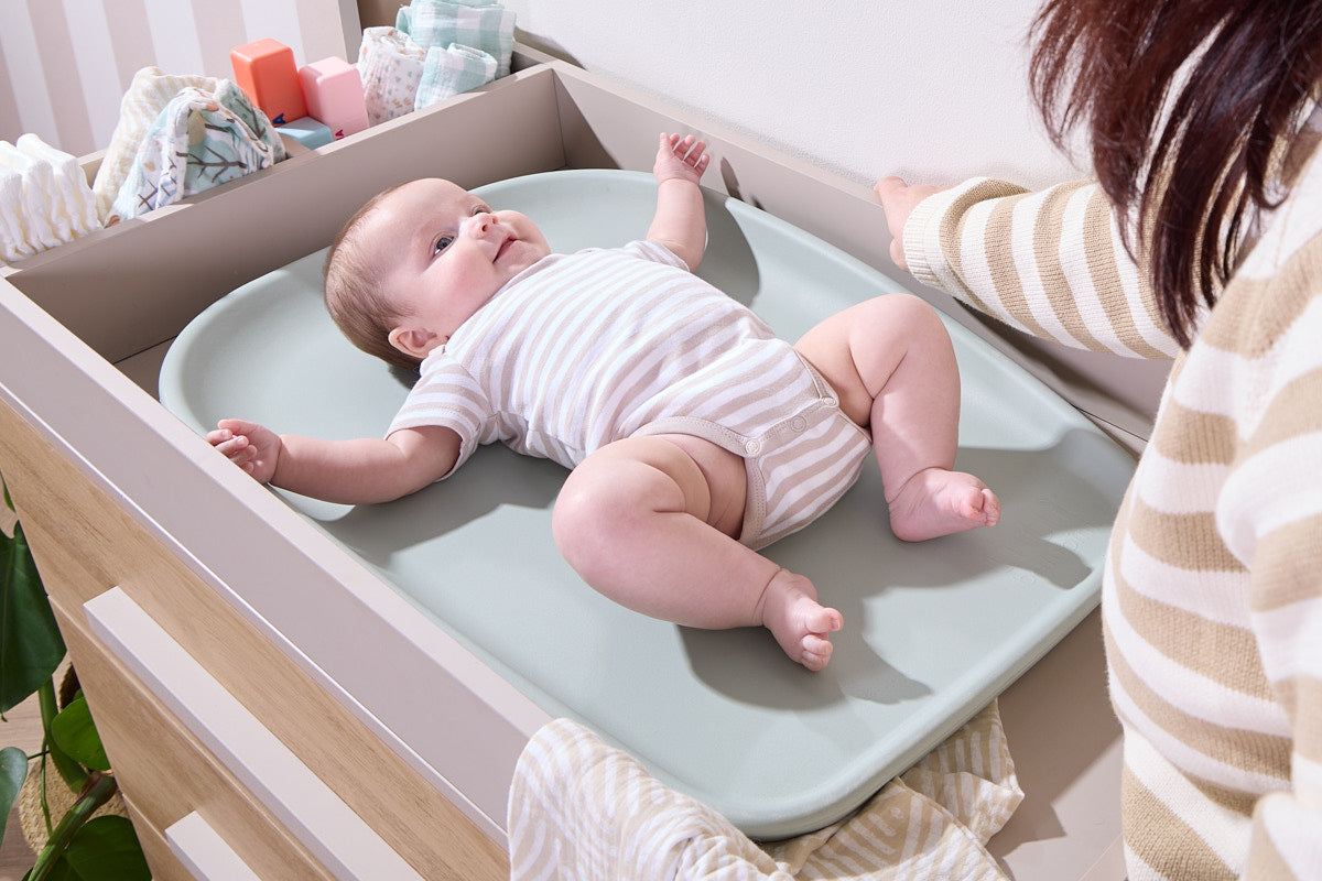 Baby lies on Cushi Mini changing mat in leaf on chest changer, showing cushioned surface, raised edges, and supportive comfort.