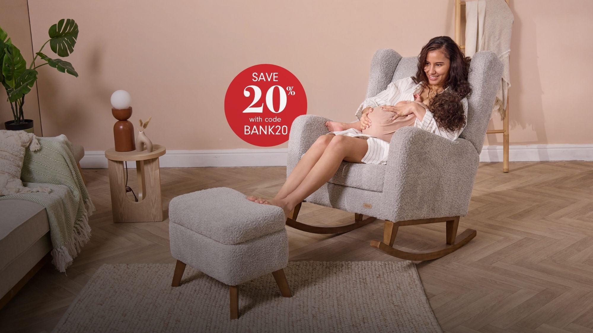 A woman sits in a light grey nursing chair with wooden rockers, holding a baby, in a styled nursery setting. A matching gray footstool is in front of the chair. In the red circle in the centre, it reads 'Save 20% with code BANK20'.