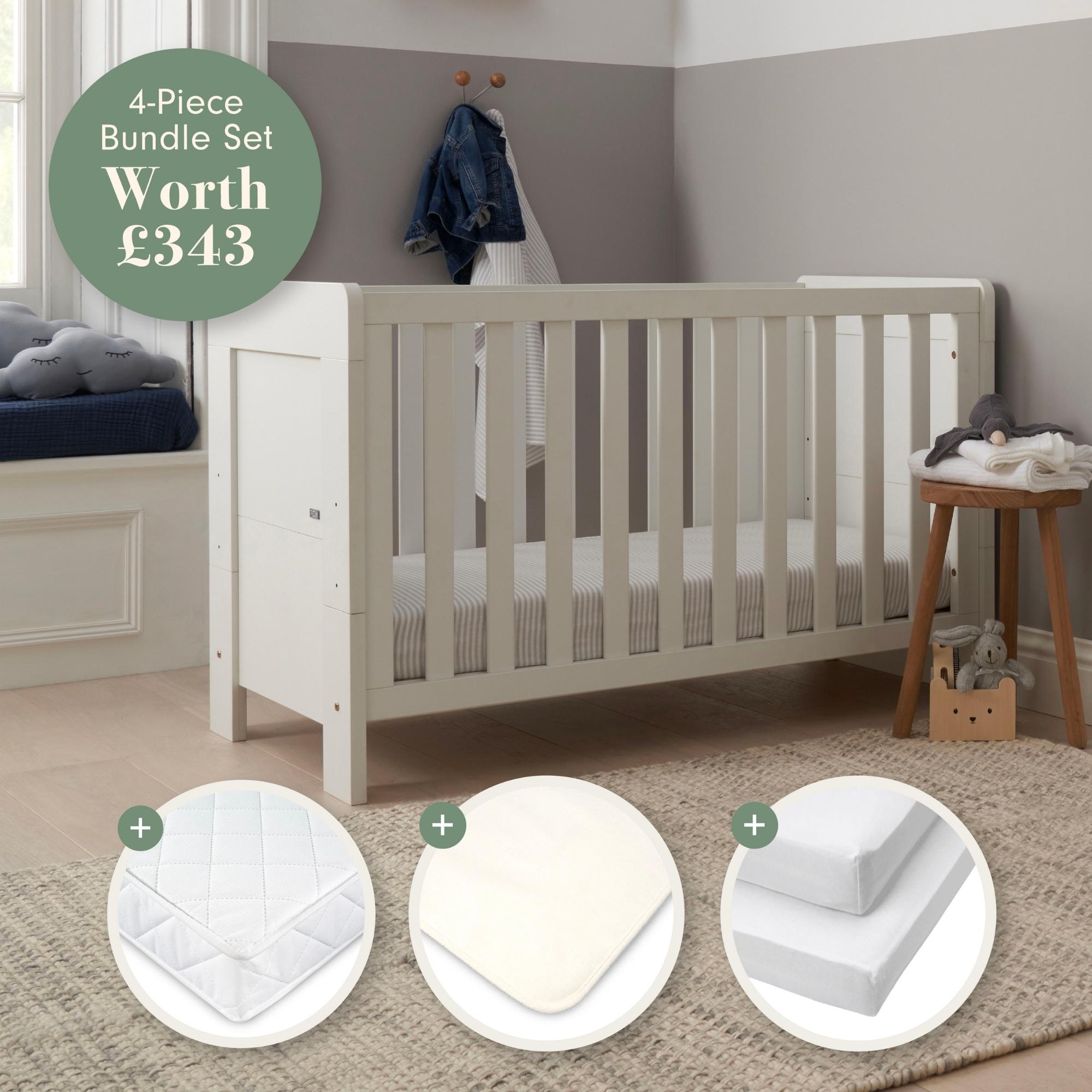 Alba Mini Cot Bed in white in a room with a mattress and baby bedding products displayed below.