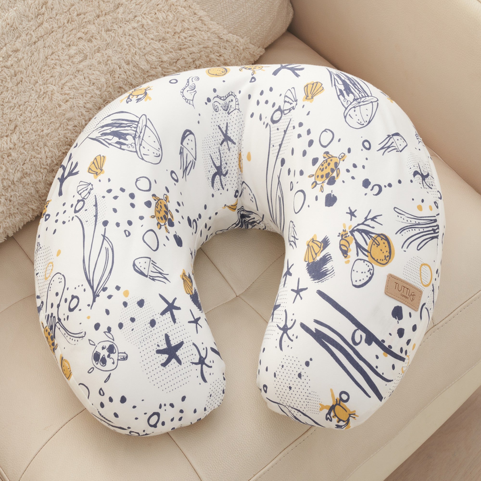 Curved feeding pillow in Our Planet print, featuring soft supportive shape and illustrated ocean-inspired pattern, styled on a neutral sofa.