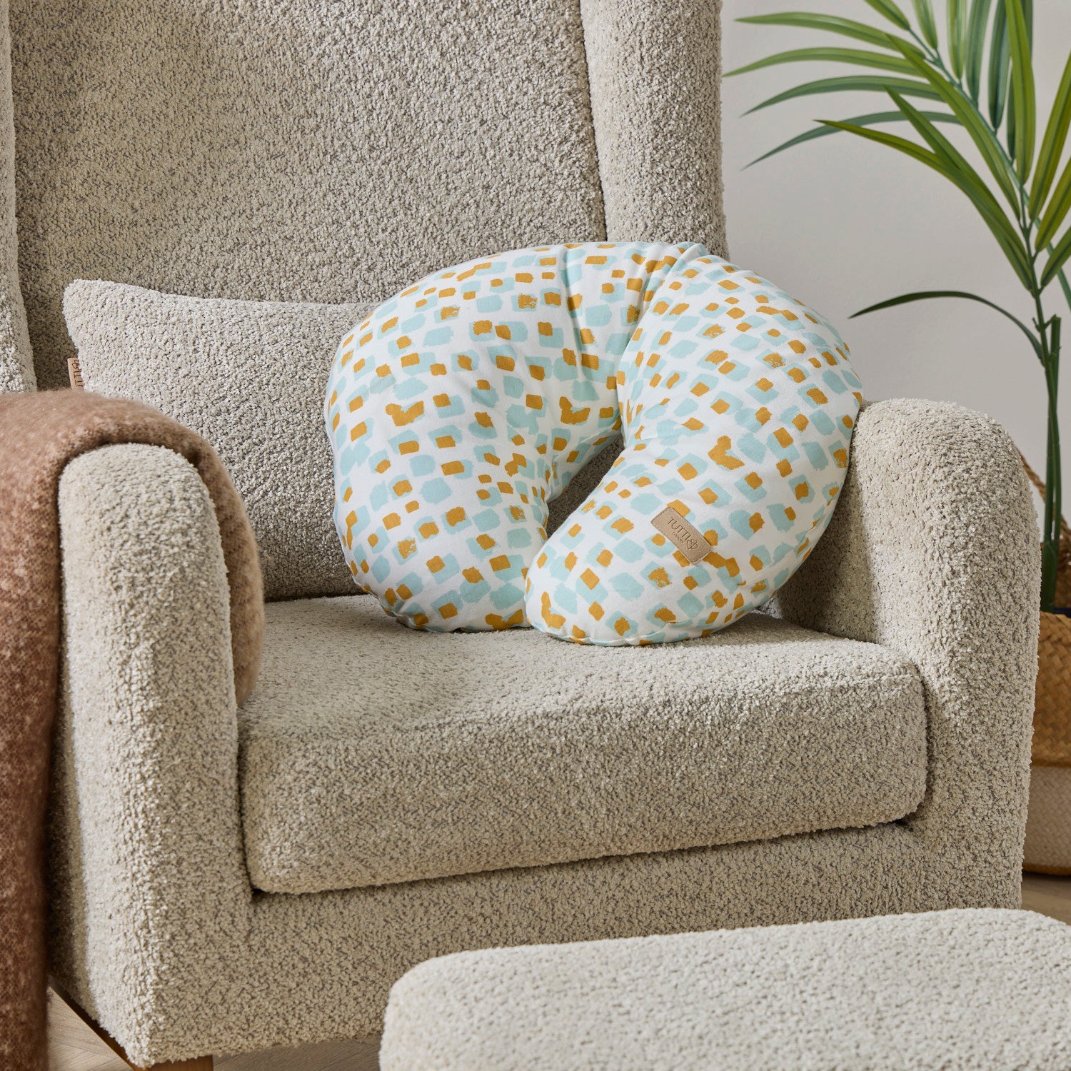Run Wild white feeding pillow with blue and orange pattern on a beige nursing chair