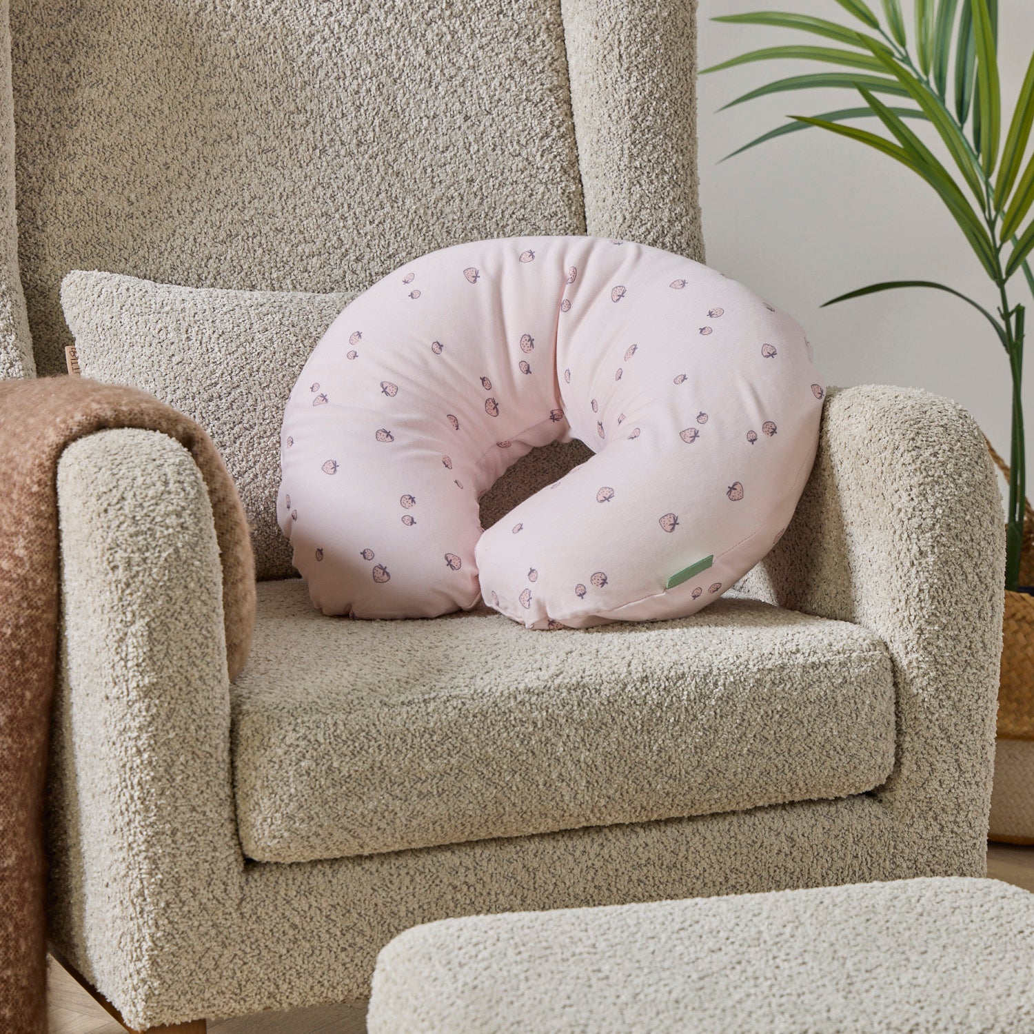 Tiny Tails pink feeding pillow with a strawberries pattern on a beige nursing chair