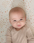 Baby wearing a beige onesie on a farm-patterned cot bed sheet from the Good Life collection.