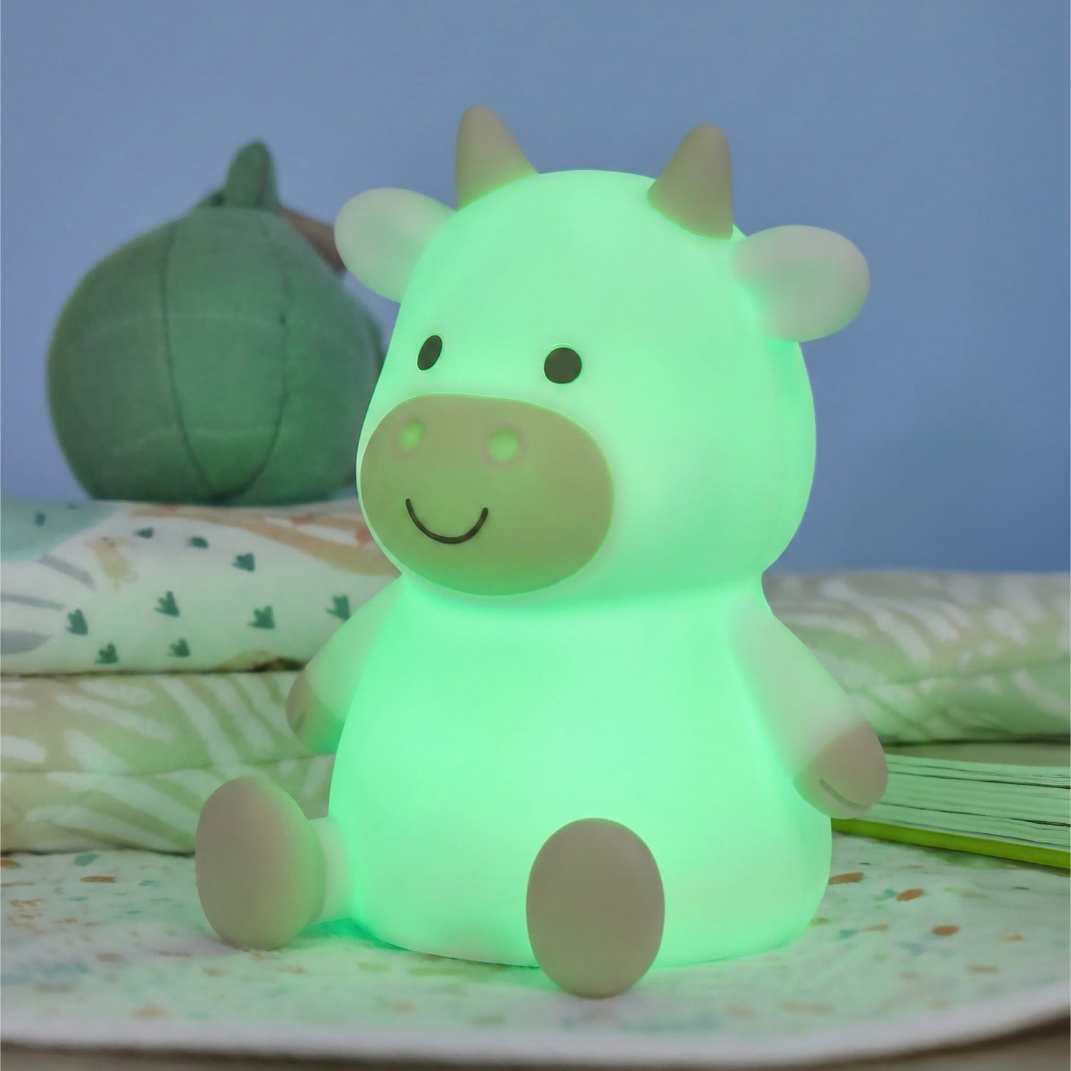 Glowing green cow-shaped night light on a soft surface with a blurred background