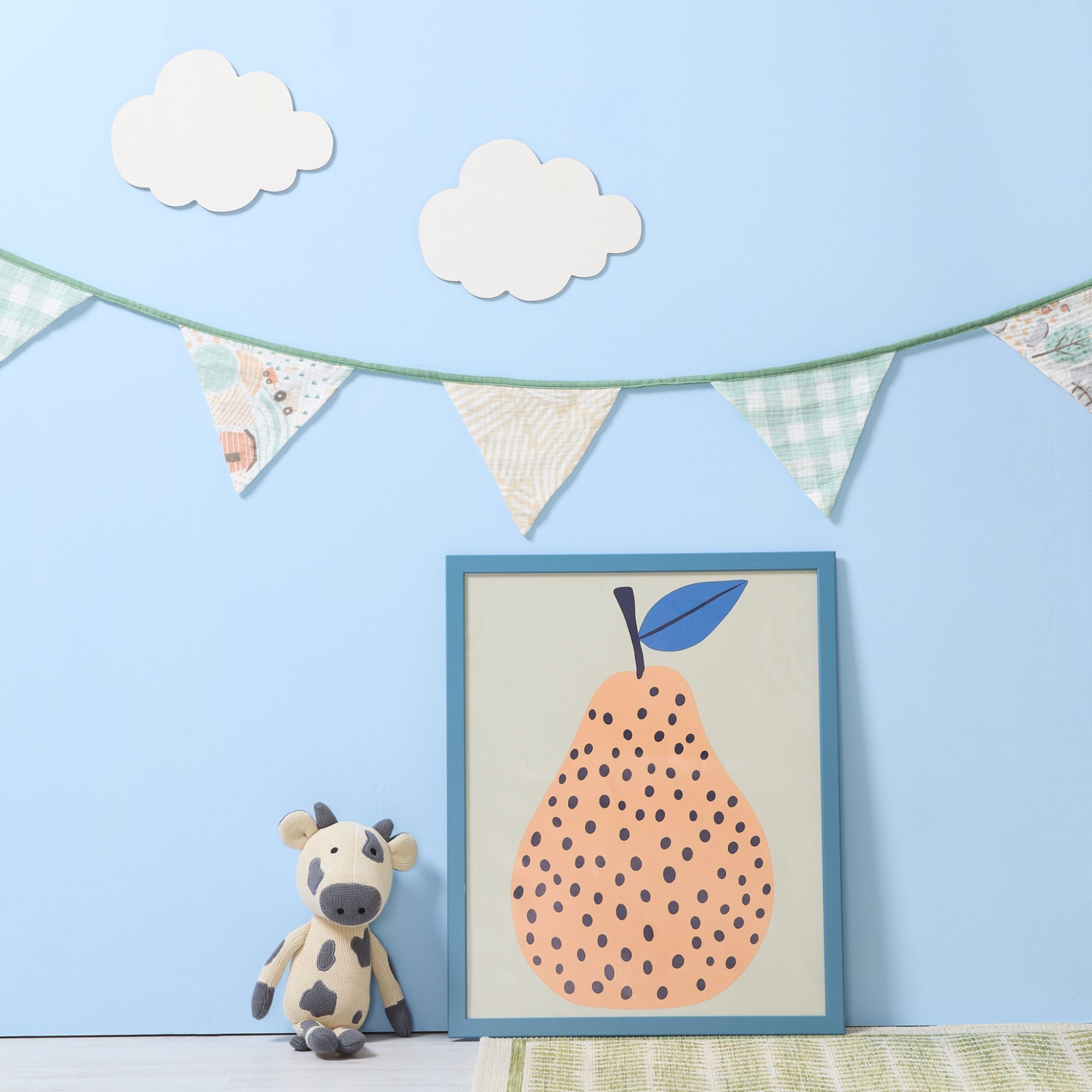 good life nursery bunting styled on blue wall above framed pear print and knitted cow toy in a soft pastel bedroom setting.