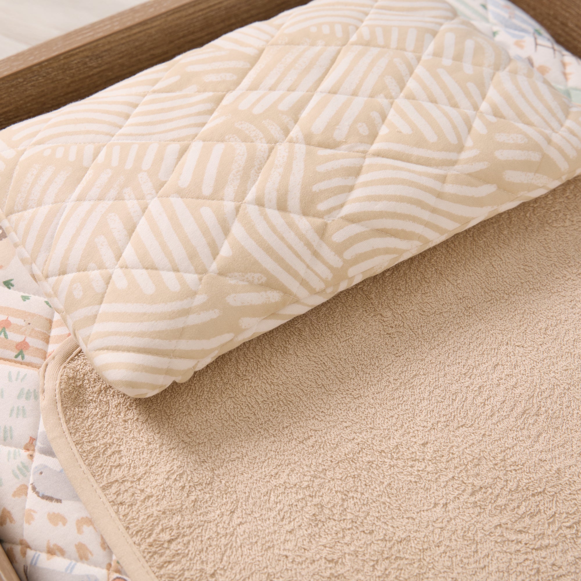 Beige quilted baby changing mat with a subtle pattern on a wooden surface