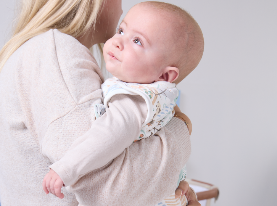 Baby wearing a sleep bag from the Good Life Collection, being held by her mother against a white background.