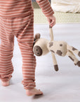 Child wearing orange and white striped pyjamas holding a Clemi cow knitted toy.