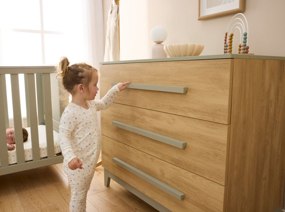 Close lifestyle view of Hallee chest changer in sage and golden oak as child reaches for smooth sage handle.