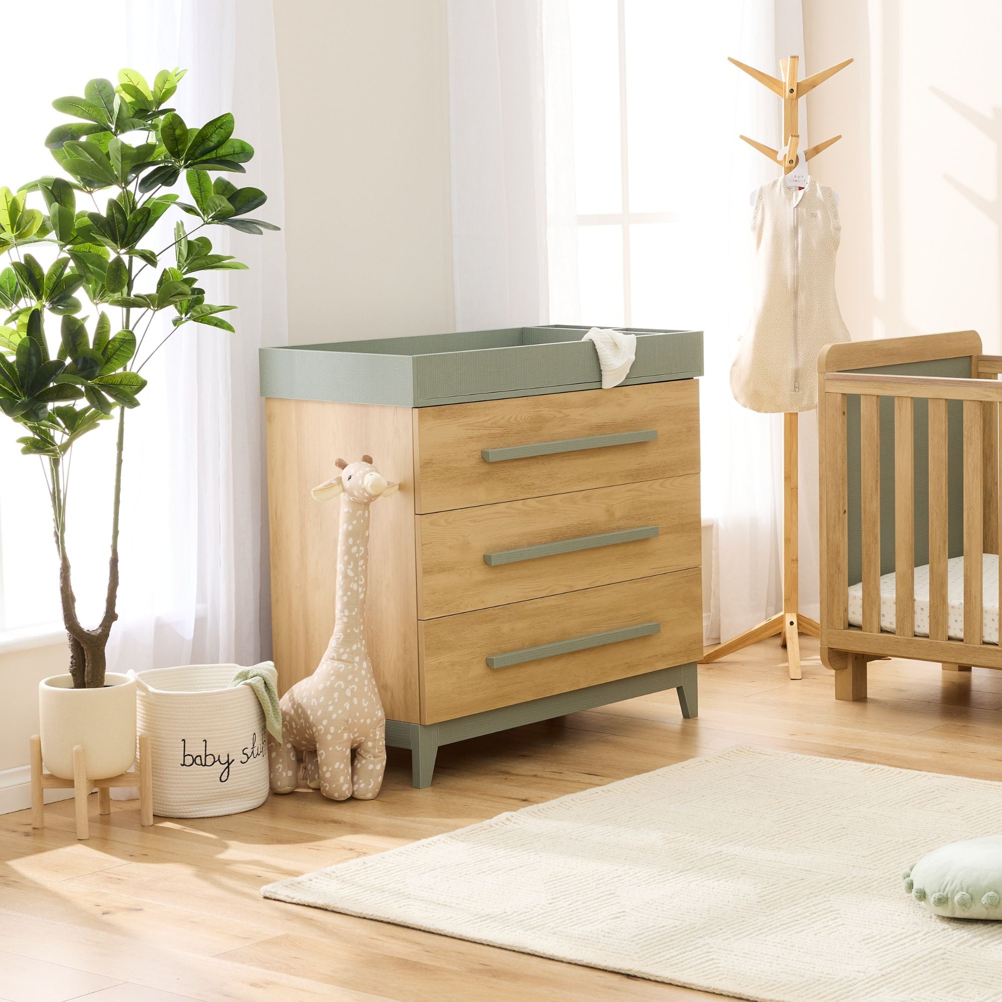 Lifestyle of hallee chest in sage weave and golden oak styled in nursery with cot, plant and soft toys on rug.